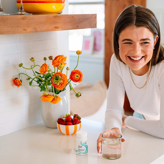 Woman sitting at a table with a vase of flowers, bowl of strawberries, and a glass of water.