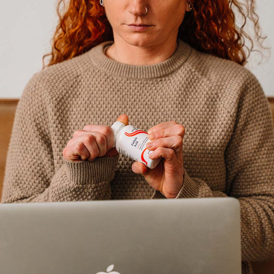 Person holding a bottle of lozenges in front of a laptop