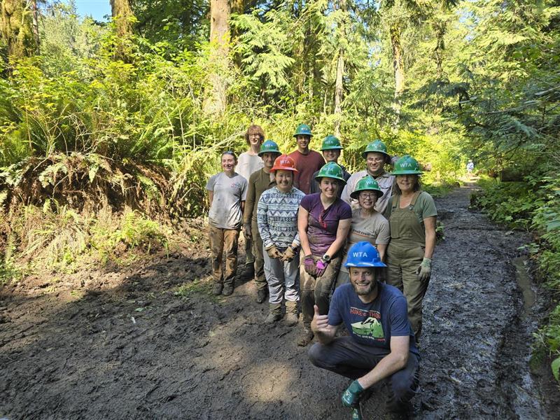 Group of people in a forest setting with muddy paths and greenery.