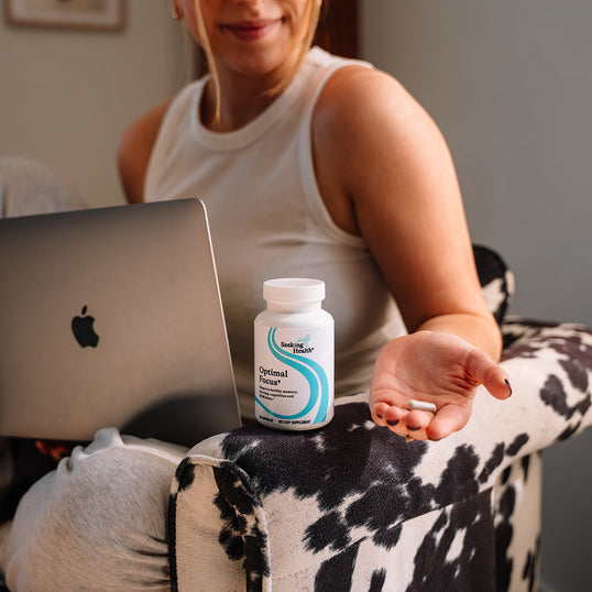 Person sitting on a couch with a laptop and a bottle of supplements